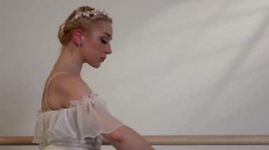 Beyaz elbiseli güzel bir balerin, beyaz güneşli bir odada dans eder. Siyah bir zemin, bir bale barının yanında.