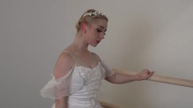 Beyaz elbiseli güzel bir balerin, beyaz güneşli bir odada dans eder. Siyah bir zemin, bir bale barının yanında.