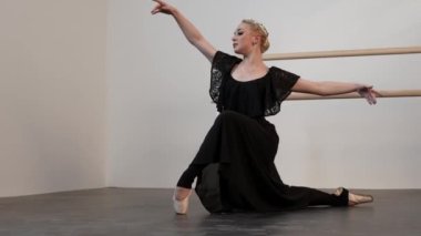 Siyah elbiseli güzel bir balerin, beyaz güneşli bir odada dans eder. Siyah bir zemin de bir bale barının yanında.