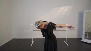 Siyah elbiseli güzel bir balerin, beyaz güneşli bir odada dans eder. Siyah bir zemin de bir bale barının yanında.