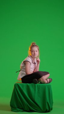 Stüdyoda poz veren liseli kız. Genç liseli kız oturup düşünüyor ve merak ediyor. Krom anahtar yeşil ekran arka planında izole edilmiş. Çalışma alanı modeli. Eğitim reklamcılığı konsepti. Dikey video.