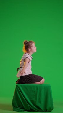 Stüdyodaki liseli kız. Oturan liseli kız, krom anahtar yeşil ekranda izole edilmiş uçak elleri gibi hareket ediyor. Çalışma alanı modeli. Eğitim reklamcılığı konsepti. Dikey video.
