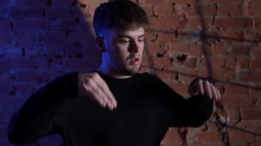 Siyah elbiseli genç adam kırmızı tuğla duvara karşı hip hop dansı yapıyor..