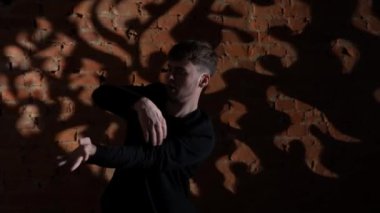 Siyah elbiseli genç adam kırmızı tuğla duvara karşı hip hop dansı yapıyor..