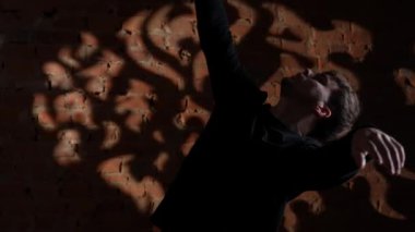 Siyah elbiseli genç adam kırmızı tuğla duvara karşı hip hop dansı yapıyor..