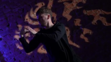 Siyah elbiseli genç adam kırmızı tuğla duvara karşı hip hop dansı yapıyor..