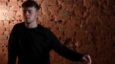 Siyah elbiseli genç adam kırmızı tuğla duvara karşı hip hop dansı yapıyor..