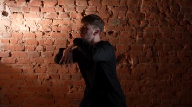 Siyah elbiseli genç adam kırmızı tuğla duvara karşı hip hop dansı yapıyor..
