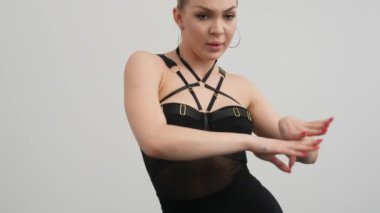 Siyah elbiseli genç bir kadın siyah zemini olan beyaz bir odada yüksek tepelerde dans ediyor..