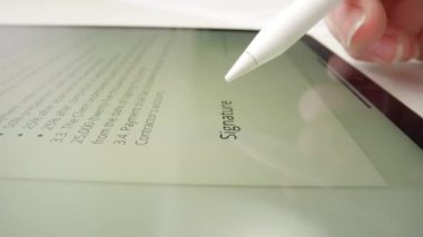 Elektronik olarak imzalanan bir belgeyi gösteren dijital tabletin yakın görüntüsü. Bir stil kalemi ekranda imzaya benzer bir mürekkep bırakır.