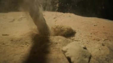 Matkap ucu kumtaşı yüzeyine nüfuz eder ve ince kum tanecikleri havaya fırlar. Metalik matkap ve dönen toz bulutu, sondaj işleminin gücü ve hassasiyeti.