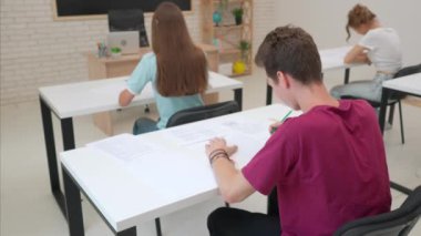 Oditoryumdaki bir grup genç kız ve erkek öğrenci. Sınıftaki liseli gençler, sınav yazan çocuklar soruları cevaplıyor, sinirli ifadeler, kağıtları fırlatıyor. Modern eğitim kavramı.
