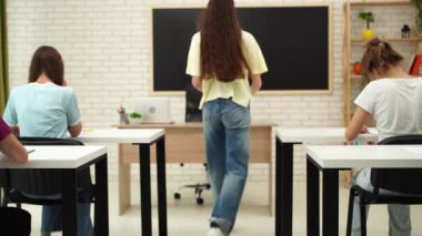 Oditoryumdaki bir grup genç kız ve erkek öğrenci. Sınıftaki liseli gençler, masalarında oturup sınavlarını bitiriyorlar, öğretmenlerin masasına yürüyüp sınav kağıtlarını yerleştiriyorlar. Modern eğitim kavramı.