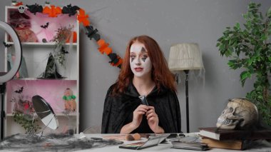 Kadın nüfuzlu kişi canlı video makyaj dersi veriyor. Evde pelerinli genç bir kadın güzellik blogcusu Cadılar Bayramı partisi makyajı için video dersi veriyor, kamerayla konuşuyor, ürkütücü gözler makyajı yapıyor..