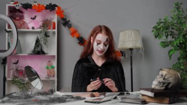 Kadın nüfuzlu kişi canlı video makyaj dersi veriyor. Evde pelerinli genç bir kadın güzellik blogcusu Cadılar Bayramı partisi makyajı için video dersi veriyor, kamerayla konuşuyor, ürkütücü gözler makyajı yapıyor..