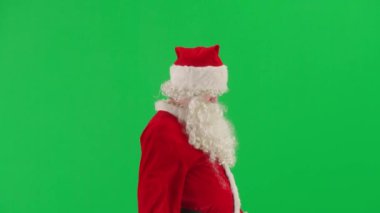Noel ve Yeni Yıl yaratıcı konsepti. Krom anahtar yeşil ekranda Noel Baba kılığında bir adam portresi. Kırmızı kıyafetli Noel Baba etrafta dolanıp insanları selamlıyor. Yan görünüm