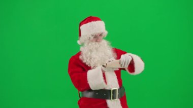 Noel ve Yeni Yıl yaratıcı konsepti. Krom anahtar yeşil ekranda Noel Baba kılığında bir adam portresi. Kırmızı kıyafetli Noel Baba kağıt rulo açar, baş parmağını kaldırarak okur..