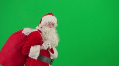 Noel ve Yeni Yıl yaratıcı konsepti. Krom anahtar yeşil ekranda Noel Baba kılığında bir adam portresi. Kırmızı elbiseli Noel Baba bir çanta dolusu hediye ve el sallıyor..