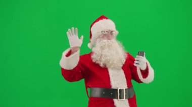 Noel ve Yeni Yıl yaratıcı konsepti. Krom anahtar yeşil ekranda Noel Baba kılığında bir adam portresi. Kırmızı kıyafetli Noel Baba arıyor. Video aracılığıyla akıllı telefondan konuşuyor..