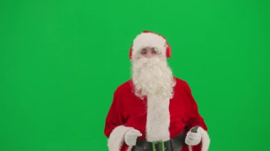Noel ve Yeni Yıl yaratıcı konsepti. Krom anahtar yeşil ekranda Noel Baba kılığında bir adam portresi. Noel Baba kırmızı kulaklıklı, akıllı telefonlu dans eden müzik dinliyor..