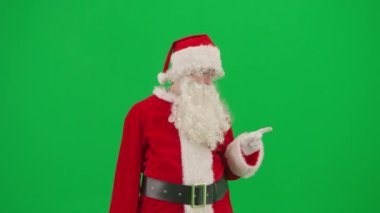 Noel ve Yeni Yıl yaratıcı konsepti. Krom anahtar yeşil ekranda Noel Baba kılığında bir adam portresi. Kırmızı kıyafetli Noel Baba boş bölgeyi işaret ediyor..