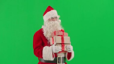 Noel ve Yeni Yıl yaratıcı konsepti. Krom anahtar yeşil ekranda Noel Baba kılığında bir adam portresi. Kırmızı kıyafetli Noel Baba hediye kutuları taşıyor ve yürüyor.