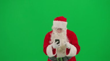 Noel ve Yeni Yıl yaratıcı konsepti. Krom anahtar yeşil ekranda Noel Baba kılığında bir adam portresi. Kırmızı kıyafetli Noel Baba elinde akıllı telefon ile haberleri okuyor..