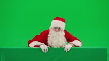 Noel ve Yeni Yıl yaratıcı konsepti. Krom anahtar yeşil ekranda Noel Baba kılığında bir adam portresi. Kırmızı kıyafetli Noel Baba boş tahtanın arkasında belirdi ve....