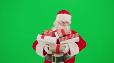 Noel ve Yeni Yıl yaratıcı konsepti. Krom anahtar yeşil ekranda Noel Baba kılığında bir adam portresi. Kırmızı elbiseli Noel Baba hediye kutuları taşıyor.
