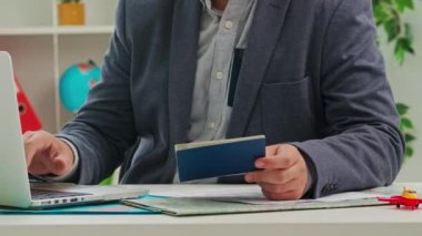 Takım elbiseli bir adam seyahat acentesinde oturuyor. Müşteri pasaportundan bilgisayara girip evrakları işlemek ve bir tur ayarlamak için veri topluyor. Kapat..
