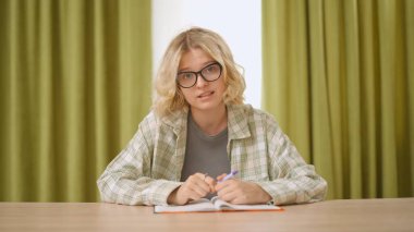 Çevrimiçi kursa katılan genç kişi. Evde çalışan, masa başında oturan bilgisayar dersini dinleyen, not defterine yazan bir üniversite öğrencisi. Modern online eğitim.