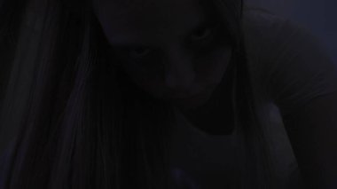 Genç bir kadın karanlıkta merdivenlerde. Beyaz elbiseli ve korkunç makyajlı ürkütücü hayalet kadın karanlık perili evde tek başına kameraya el feneriyle bakıyor, kapat. Cadılar Bayramı korku konsepti.