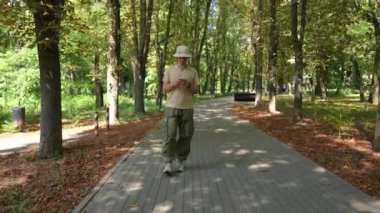 Elinde cep telefonuyla parkta yürüyen genç bir adam. Sıradan kıyafetler giymiş bir adamın telefonuna mesaj yazışının ön görüntüsü. Eğlence ve aktif yaşam tarzı kavramı.