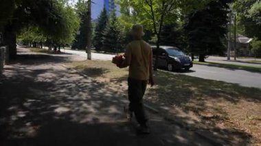 Elinde bir hediye kutusuyla şehrin sokaklarında yürüyen genç bir adam. Güneşli bir yaz gününde şehrin kaldırımında yürürken günlük giysiler giymiş bir adamın arka görüntüsü. Tatil kavramı...