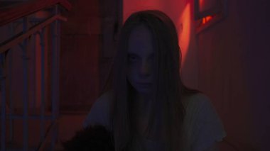 Genç bir kadın karanlıkta merdivenlerde. Beyaz elbiseli ve korkunç makyajlı ürkütücü hayalet kadın karanlık perili evde tek başına merdivenlerde kameraya bakar, kapat. Cadılar Bayramı korku konsepti.