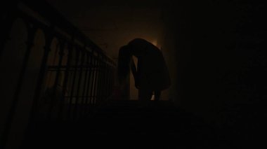 Genç bir kadın karanlıkta merdivenlerde. Beyaz elbiseli ve korkunç makyajlı ürkütücü hayalet kadın karanlık perili evde merdivenlerde tek başına duruyor. Cadılar Bayramı korku reklam konsepti.