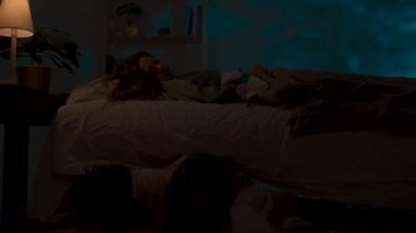 Genç bir bayan karanlıkta evde kestiriyor. Karanlık bir dairede yatakta uyuyan bir kadın, yatağın altında saklanan bir canavar, yerde sürünen ürkütücü bir kız kameraya bakıyor. Cadılar Bayramı korku konsepti.