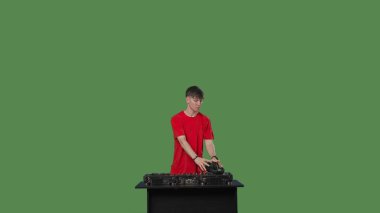 DJ masasının arkasında ustaca müziği karıştıran parlak kırmızı tişört giymiş erkek DJ, canlı müzik etkinliğinin yüksek enerjili atmosferini aktarıyor. Yeşil ekran krom anahtarı