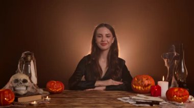 Büyücülük yapan mistik kadın büyücü. Cadılar Bayramı gotik cadı falcısı masada otururken iyi bir el işareti gösteriyor, olumlu bir şekilde başını sallıyor. Sihirli cadılar bayramı kavramı.