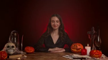 Büyücülük yapan mistik kadın büyücü. Cadılar Bayramı gotik cadı falcısı masada otururken iyi bir el işareti gösteriyor, olumlu bir şekilde başını sallıyor. Sihirli cadılar bayramı kavramı.