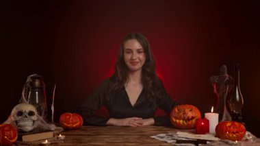 Büyücülük yapan mistik kadın büyücü. Masada oturan gotik cadı falcı kadın başparmağını bir jest gibi kaldırıyor ve olumlu bir şekilde başını sallıyor. Sihirli cadılar bayramı kavramı.