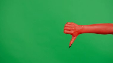 Stüdyoda jestler gösteren korkunç bir el. Korkunç cadılar bayramı canavarı kırmızı tırnaklı el siyah tırnaklı kötü baş parmak işareti gösteriyor, yeşil ekran arka planında izole edilmiş, çalışma alanı modeli..