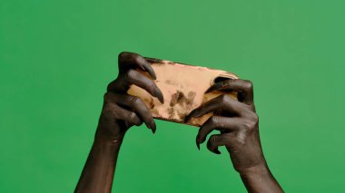 Stüdyoda jestler gösteren korkunç bir el. Korkunç cadılar bayramı canavarı siyah tırnaklı el boyası akıllı telefonda video oyunu oynuyor, krom anahtar yeşil ekran arka planında izole edilmiş, çalışma alanı modeli