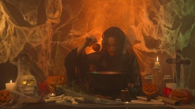Siyah elbiseli cadı korkunç mutfaktaki kazandan zehirli elmayı balkabakları ve insan kemikleriyle çekiyor. Etrafı dumanla kaplanmış genç bir kadın elmaya bakıyor, şeytanca gülümsüyor. Cadılar Bayramı Konsepti.