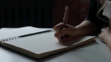 Kağıt üzerinde kadın metni. Masada oturan ve yazan bir kadın, kalemle kağıtlara notlar alan, notlar ve fikirler yazan, el yazısını yakın çekim yapan bir kadın..