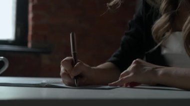 Kağıt üzerinde kadın metni. İş kadını büro masasında oturmuş kalemle notlar alıyor. Konsantre olmuş, düşüncelerini ve planlarını yazıyor. Yakın çekim..