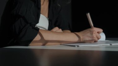 Kağıt üzerinde kadın metni. İş kadını büro masasında oturmuş kalemle notlar alıyor. Konsantre olmuş, düşüncelerini ve planlarını yazıyor. Yakın çekim..