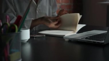 Kağıt üzerinde kadın metni. İş kadını ofis masasında dizüstü bilgisayarla oturuyor. Süt defterine kalemle notlar yazıyor. Düşüncelerini ve fikirlerini yazan biri..
