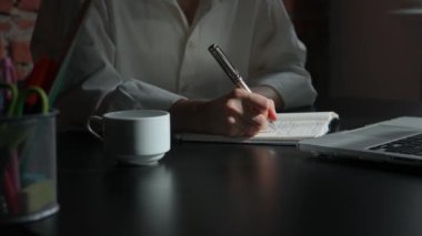Kağıt üzerinde kadın metni. İş kadını ofis masasında dizüstü bilgisayarla oturuyor. Süt defterine kalemle notlar yazıyor. Düşüncelerini ve fikirlerini yazan biri..