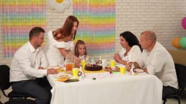 Mutlu çok nesilli aileler doğum günlerini kendi evlerinde kutlarlar. Annem doğum günü pastasını doğum günü kızına hazırlarken herkes masanın etrafında otursun. Tatil ve kutlama konsepti.